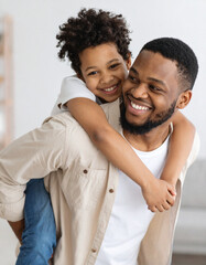 Obraz premium Mature father resting with his young son on the sofa at home, spending quality family time indoors, portrait of happy parenthood and cozy domestic life.
