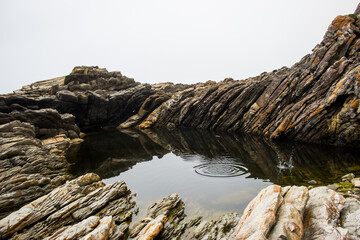 Fototapeta premium Skipping rocks on a sheltered, calm rock pool among the tilted, jagged rocks of the Tsitsikamma Coastline, South Africa.
