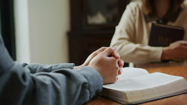 Two people praying together with open Bible indoors