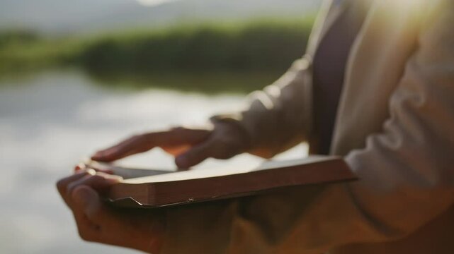 Hand reading Bible outdoors during peaceful sunset