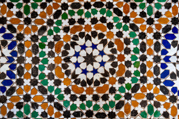 Traditional Moroccan zellige mosaic with geometric star patterns in Marrakesh, intricate Islamic tile artwork in green, blue, ochre and black, representing authentic North African craftsmanship.