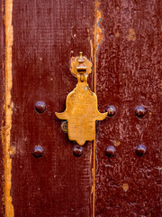 Hamsa-shaped brass door knocker on a traditional wooden door in Marrakesh, Morocco, showcasing historic craftsmanship, cultural heritage, spiritual symbolism and authentic oriental architecture.