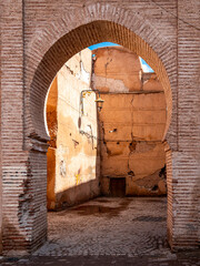Ancient arched gateway and old crumbling walls in a historic alley of Marrakech, Morocco, authentic architecture with textured stone bricks, weathered surfaces and sunlight creating dramatic shadows.