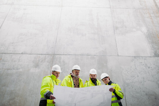 Team of engineers and construction workers reviewing blueprints, building site.
