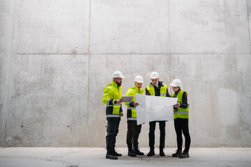 Team of engineers and construction workers reviewing blueprints, building site.