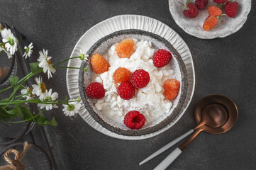 Creamed cottage cheese with raspberries. An easy healthy breakfast. A bowl filled with grainy, creamy cottage cheese is garnished with bright yellow and red raspberries. Top view