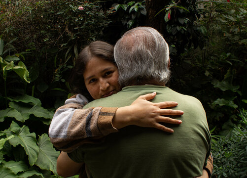 Hija le da un caluroso abrazo a su padre en medio de un jard&iacute;n.