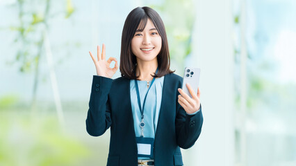 スマートフォンを持ってOKポーズをする笑顔の女性