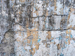 An old weathered plastered wall with cracks and unevenness. Water stains and traces of old paint of different colors are visible.