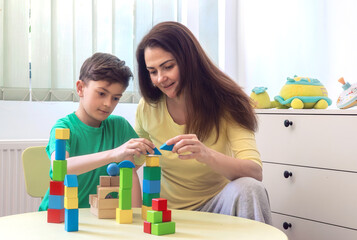 Happy young boy and woman playing with colorful wooden blocks at home. Concept of early childhood...