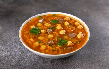 Bowl of Moroccan harira soup with chickpeas, beef, lentils and fresh parsley on grey background. Middle East cuisine.