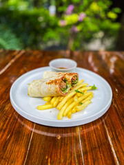 A beautifully arranged plate of golden French fries served with freshly rolled spring rolls, garnished with herbs and sauces for enhanced flavors.