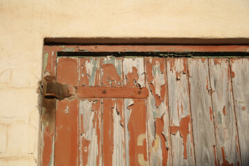 Old wooden door hanging on rusted hinges with a damaged wall
