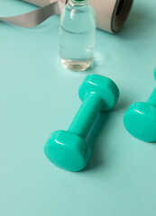 Sport or workout concept flat lay with blue dumbbells, yoga mat on the blue teal background. Close up