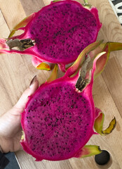 Hand holding sliced pink dragon fruit with black seeds on a wooden cutting board, showcasing...