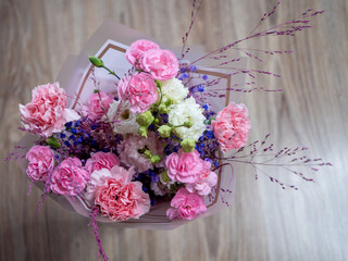 Bouquet with pink carnations, white lisianthus, purple statice, and decorative grass on a wooden floor background.