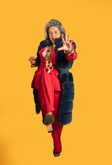 Fashionable senior woman walking and reaching out on yellow background