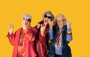 Three senior women making rock and roll hand gesture on yellow background