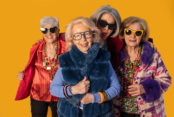 Four stylish senior women posing together on yellow background