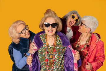 Obraz premium Four stylish senior women showing fashion and happiness on yellow background