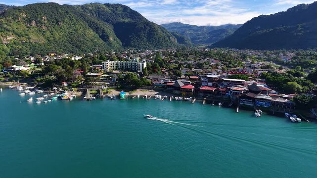 Beautiful cinematic aerial view os the Panajachel town surrounded by Toliman and Atitlan volcanoes, next to the Atitlan lake its piers and traditional fisher and tourist boats - Guatemala