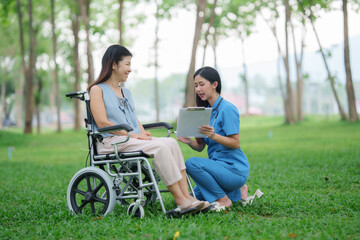 Asian nurse asks elderly female patient in wheelchair to sign insurance policy in park