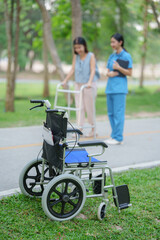 Fototapeta premium Elderly white woman sitting in wheelchair with young Asian nurse in green grass park