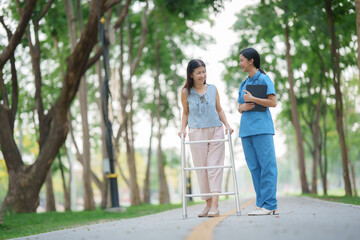 Fototapeta premium Elderly white woman sitting in wheelchair with young Asian nurse in green grass park