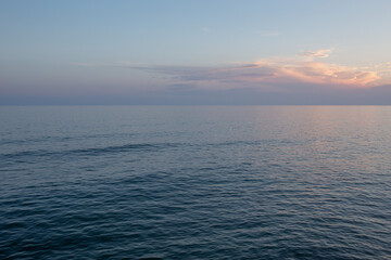 A calm twilight settles over the quiet Mediterranean shoreline. Gentle waves lap the sand, and pastel hues fill the sky as evening falls on the peaceful, nearly deserted beach.