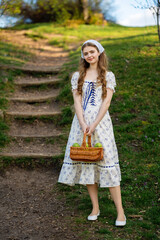 Fine art portrait of a young woman wearing light dress walking in a summer field with a basket of...