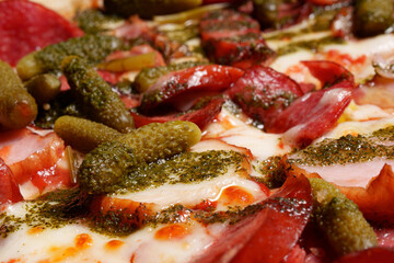 Italian pizza, peppers, gherkins, pepperoni and salami close-up. Baked.