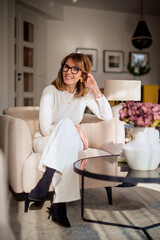Cheerful woman sitting on the armchair in her living room and smiling