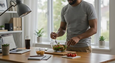 A man at a desk with a laptop prepares a fresh salad for lunch in his home office setting.