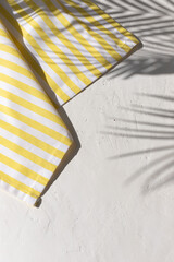 White plaster background with yellow striped pattern napkin or towel with tropical palm leaves...