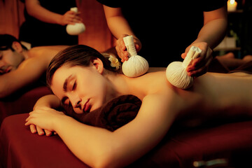 Hot herbal ball spa massage body treatment, masseur gently compresses herb bag on couple customer...