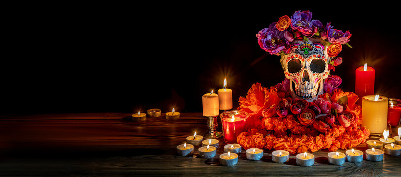 Skull with decor for the holiday Day of the Dead. Dia de los Muertos altar surrounded by ornamented calavera Catrina, candles, flowers in the darkness. All Saints' Day evening