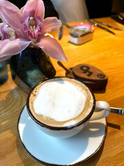 Cappuccino and orchid arrangement in cozy cafe setting for coffee shop, interior design, floral services concept