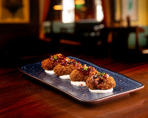 portion of mini croquettes with 4 pieces on parmesan cream in close-up with blurred restaurant in...