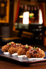 portion of mini croquettes with 4 pieces on parmesan cream in close-up with blurred pub in the background