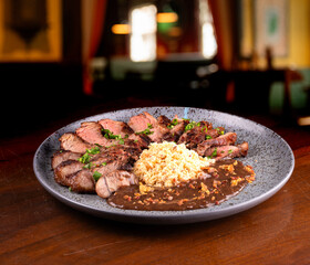 sirloin steak cut into strips served with farofa and wine sauce with blurred pub in the background