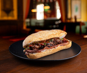 duck magret sandwich on italian baguette with bacon and spices and blurred pub background