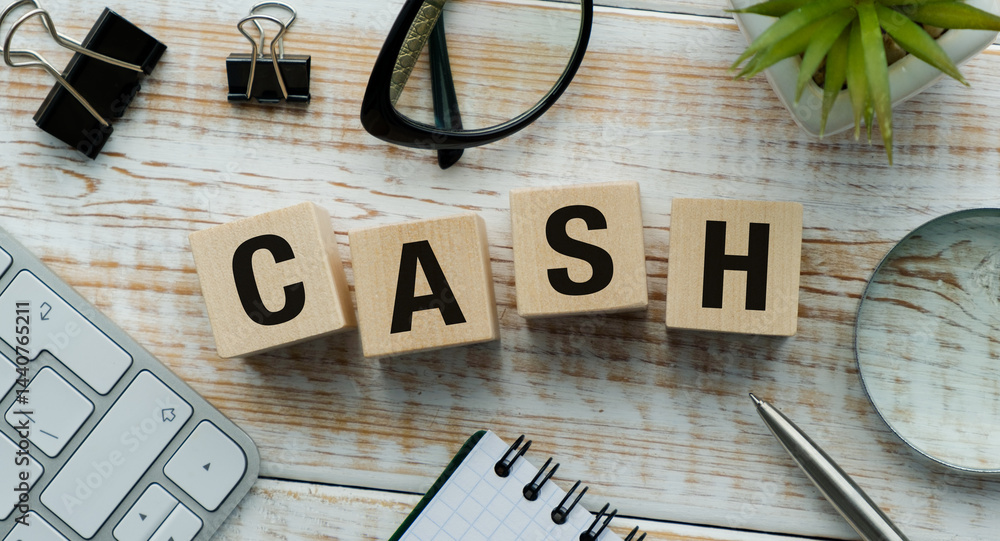 Poster a wooden block with the word cash written on it is on a desk with a keyboard