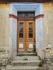 Old wooden door in Cyprus with heavy wear, cracked and faded paint, and rusty metal details....