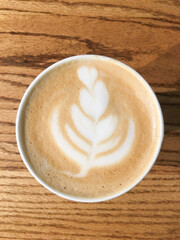 Top view of a beautifully crafted latte with elegant leaf latte art on creamy foam, served in a cozy coffee shop. Perfect for themes of cafe culture, relaxation, and artisanal beverages