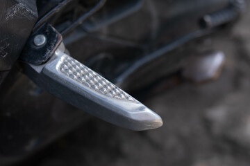 Close up of a motorcycle footrest or footpeg, showing a metal surface with grip texture used for rider foot support and stability
