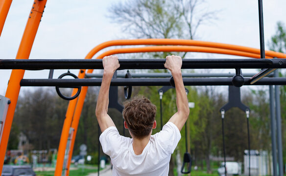 Young Man doing pull-ups outdoors. Young man training upper body strength with pull-ups on an outdoor fitness structure