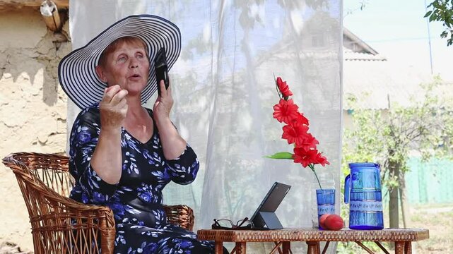 An elderly woman eats a peach while talking on a mobile phone. - Powered by Adobe