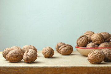 Walnuts in shell lying separately, some in bowl on wooden surface on light blue background. Super foods concept.