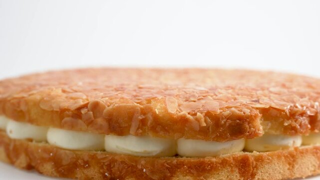 Round honey cake with almonds and white filling. Close-up of the cake rotating on a white background.