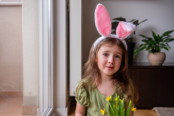 Adorable preschool girl wearing festive Easter bunny ears is joyfully holding a vibrant bouquet of...